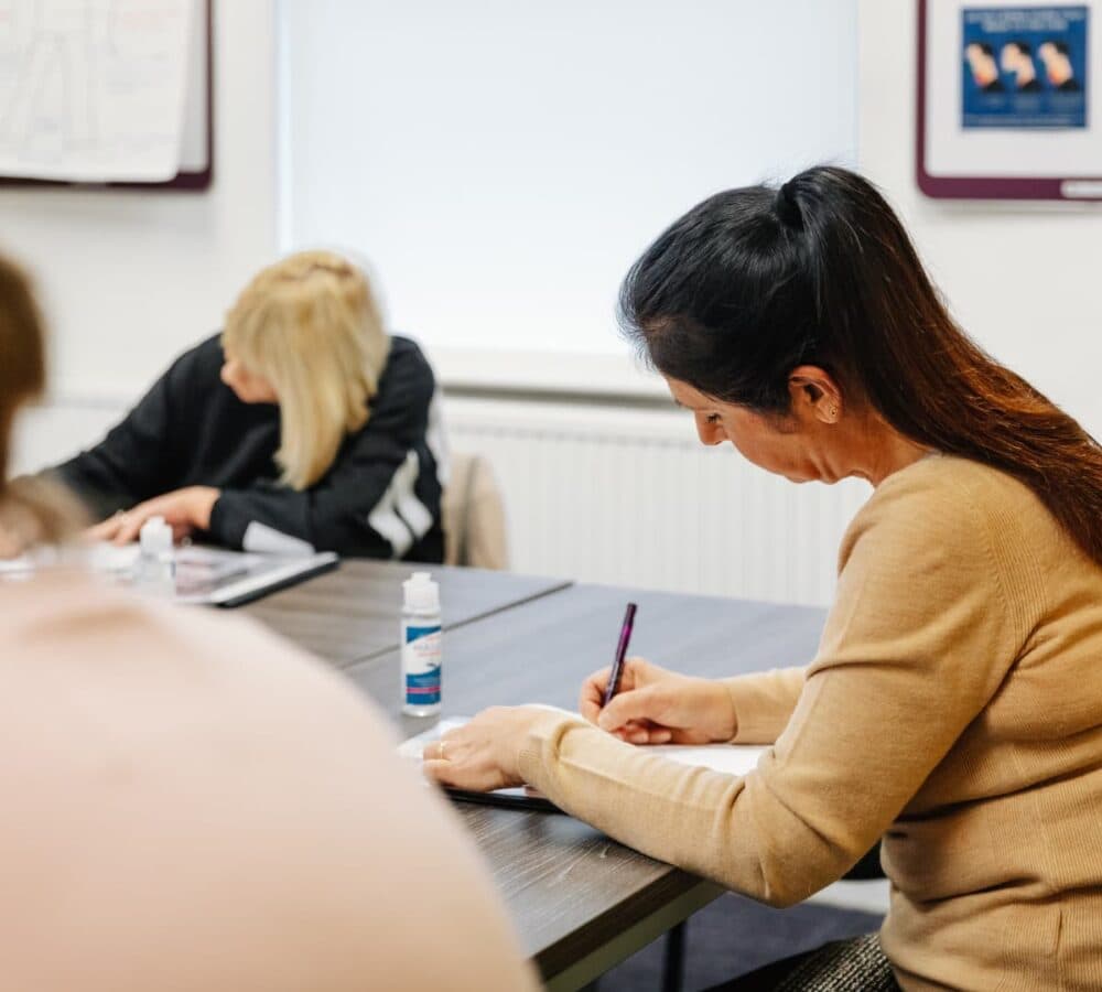 Women sitting down while writing on a paper using a desk