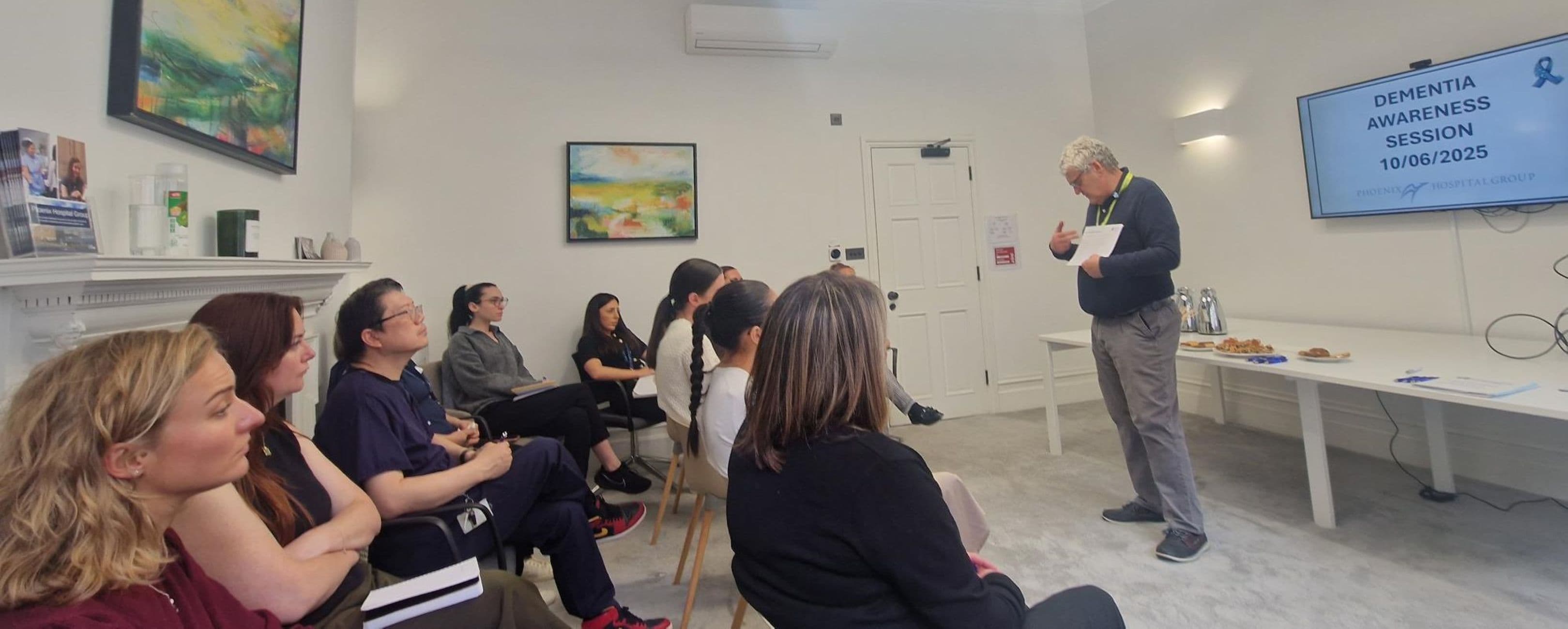 A group listens to a speaker during a Dementia Awareness Session in a bright, modern room. - Home Instead