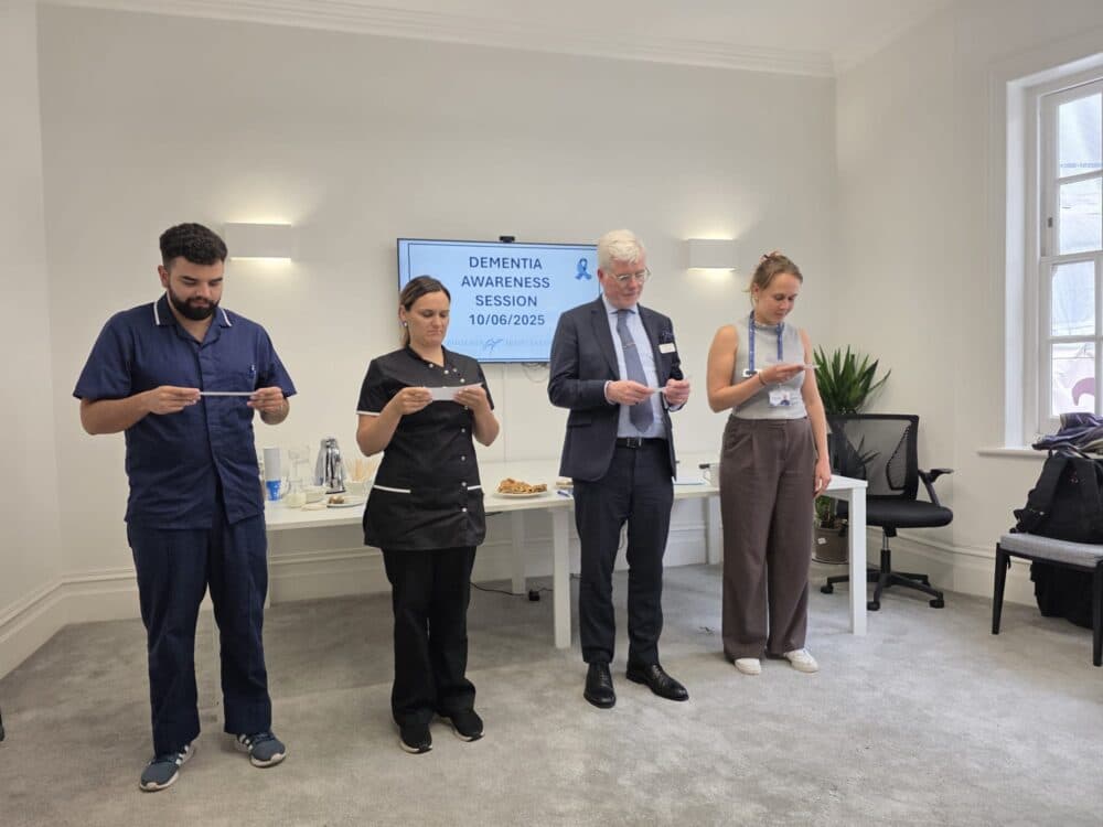Four people stand reading from cards at a dementia awareness session in a modern, bright meeting room. - Home Instead