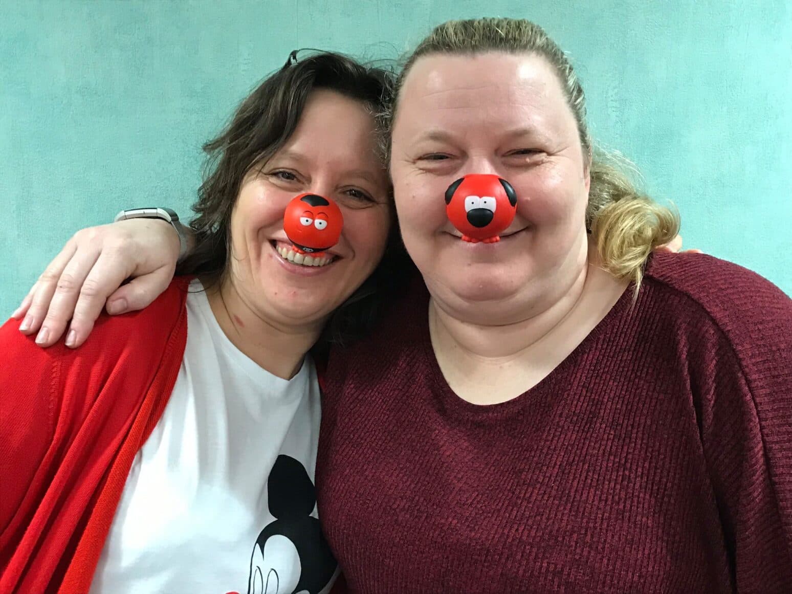 Margaret (left) and Lisa (right) stand together, smiling warmly. Lisa is holding a certificate, celebrating a special achievement.