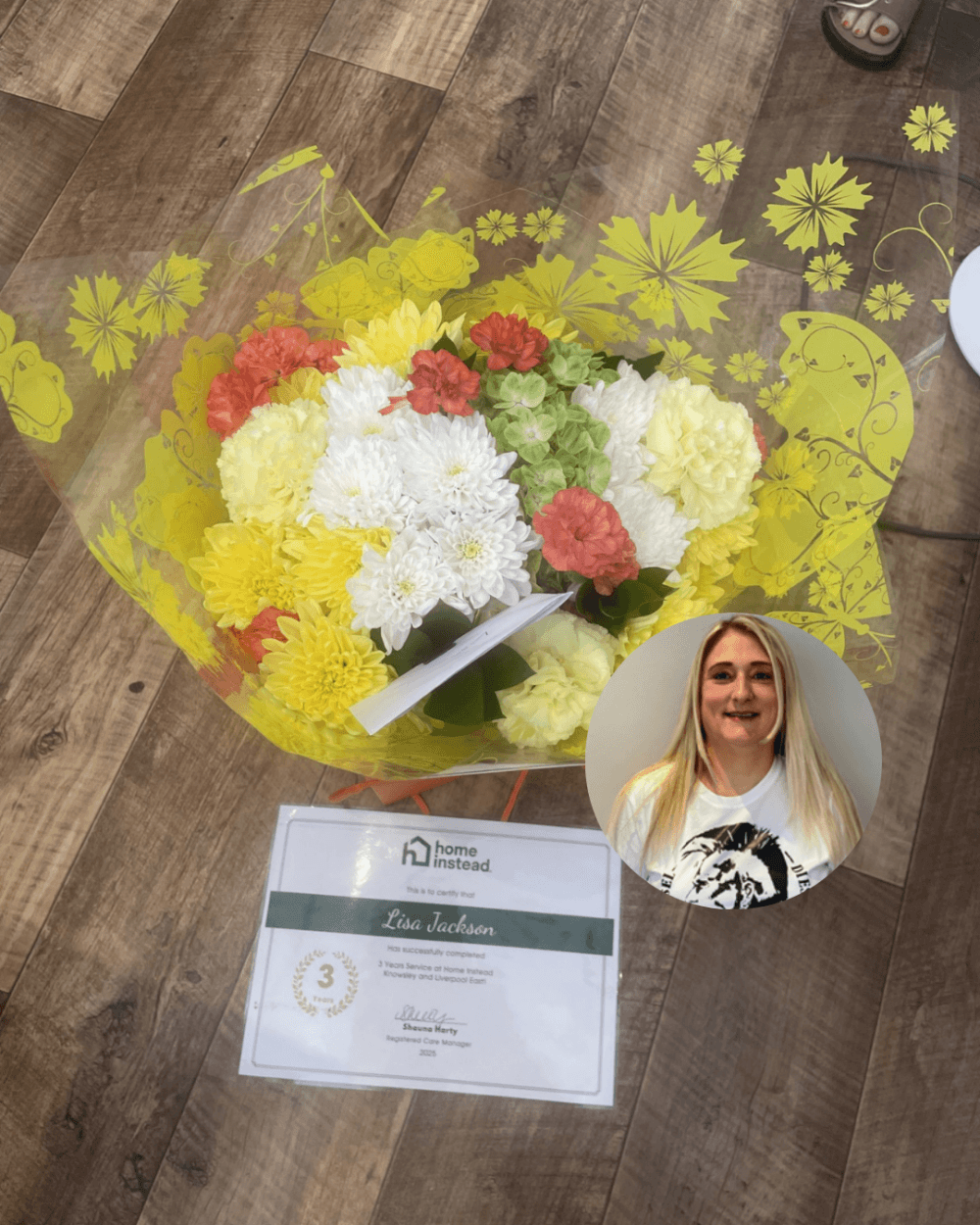 A bouquet, certificate, and headshot of a smiling woman on a wooden floor. - Home Instead