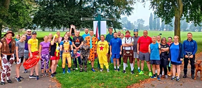 A group of people in colorful costumes pose together outdoors in a park on a cloudy day. - Home Instead