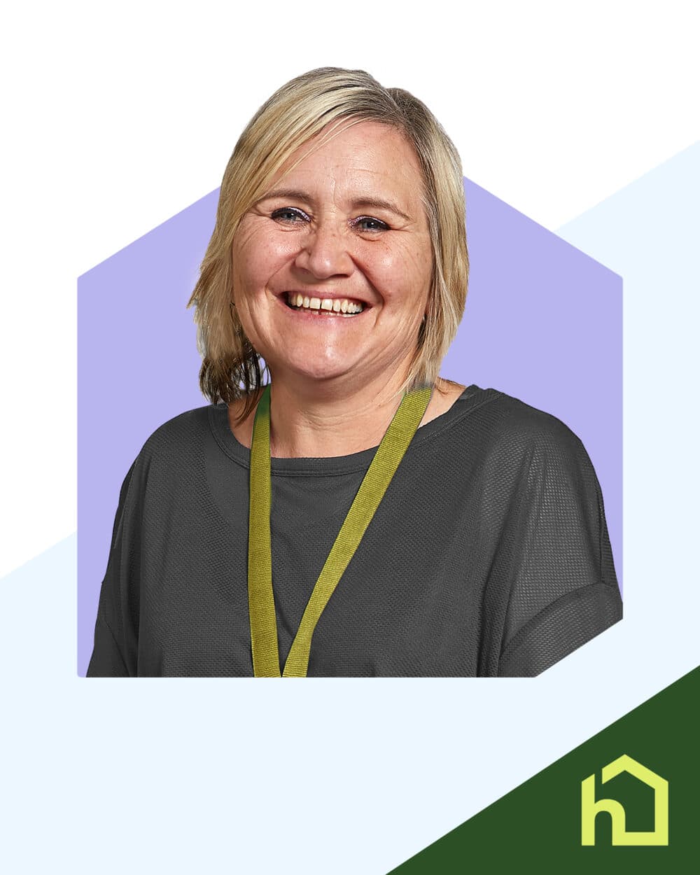 Smiling woman with blonde hair wearing a dark shirt and green lanyard, in front of a purple hexagon background. - Home Instead