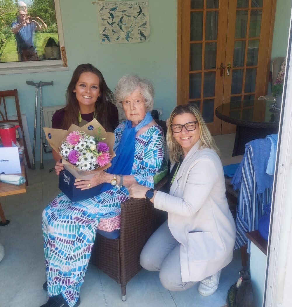 client, field care supervisor and deputy care manage posing for a photo, client holding flowers