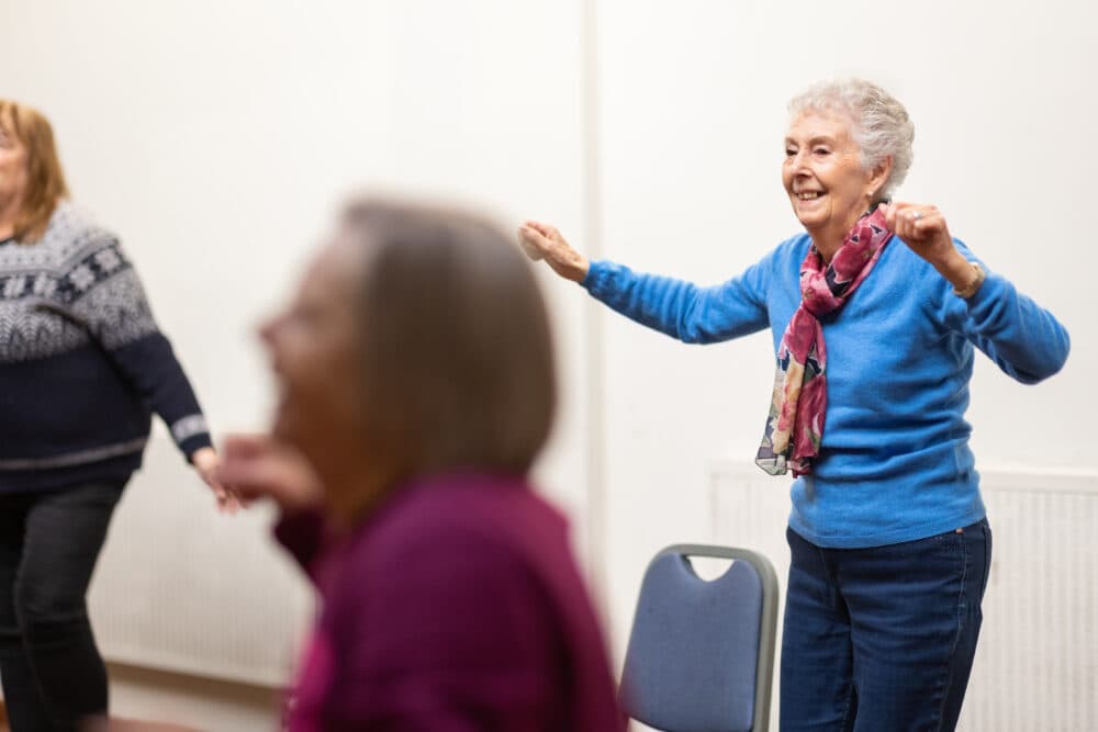 Elderly women smiling and exercising together in a brightly lit room. - Home Instead