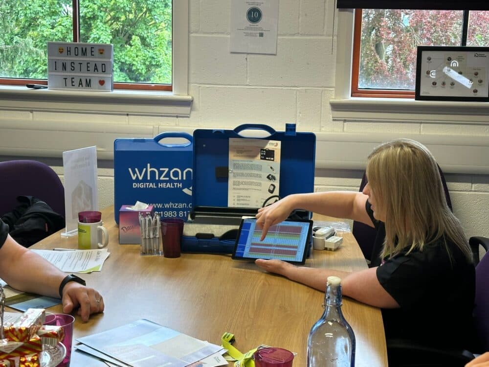 A woman points at a tablet screen during a meeting in an office with medical equipment on the table. - Home Instead