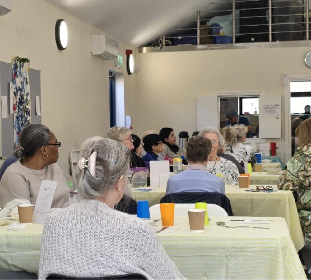 People chatting together inside the hall with long tables and tablecloths and cups