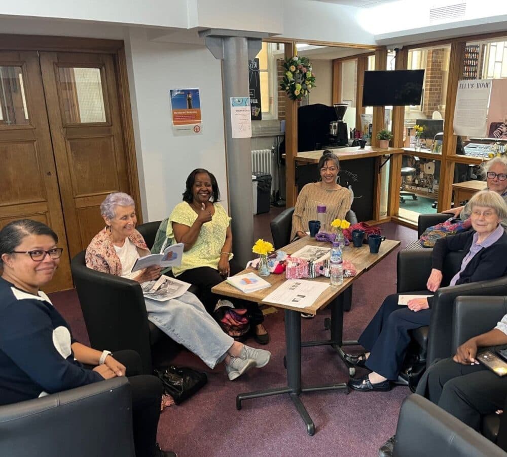 Group of people discussing around the table with some manuals, drinks and cups all are smiling inside the office