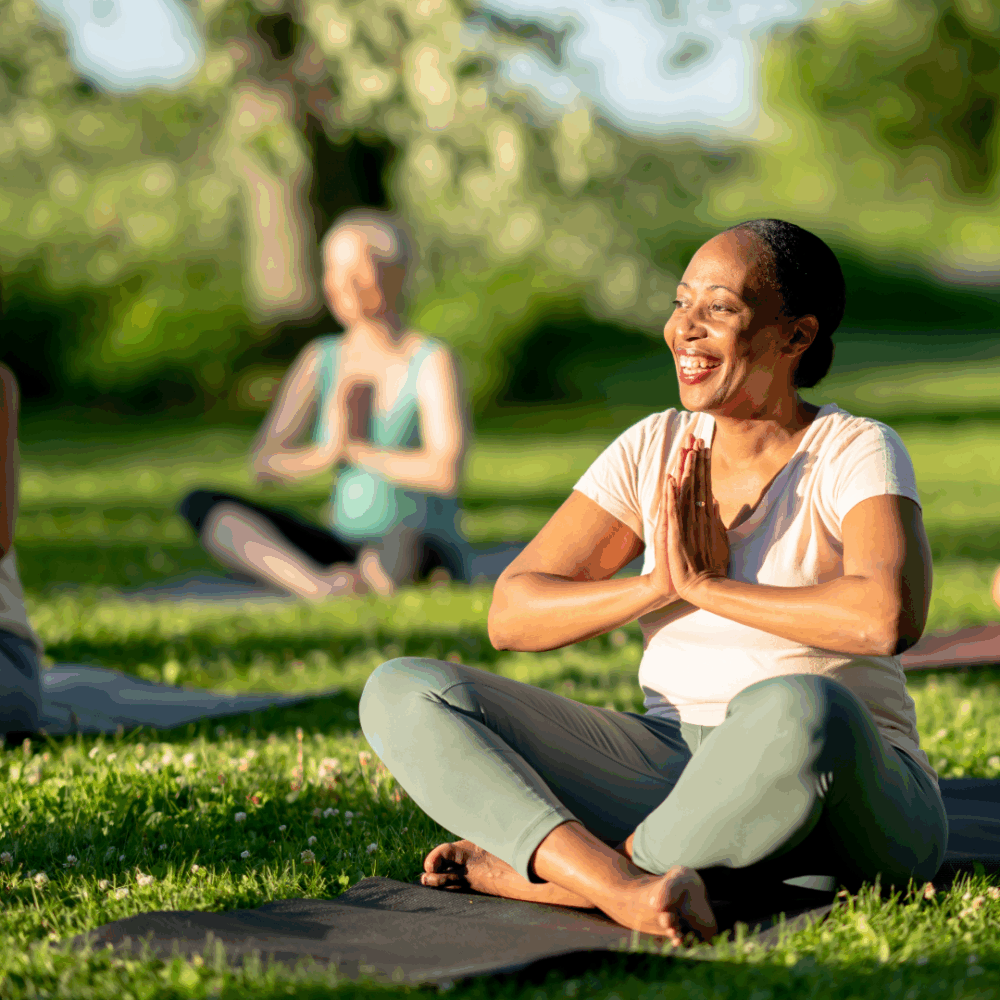 Smiling senior woman practicing seated yoga outdoors in a group class