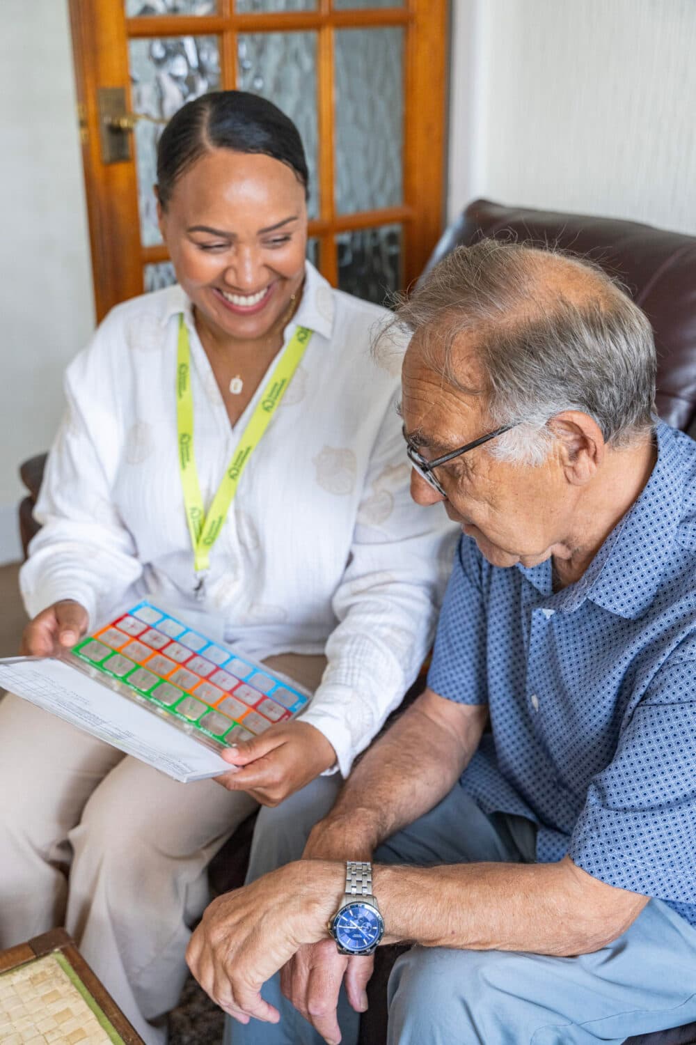 A woman shows a colorful chart to an elderly man while they sit together and smile in a living room. - Home Instead