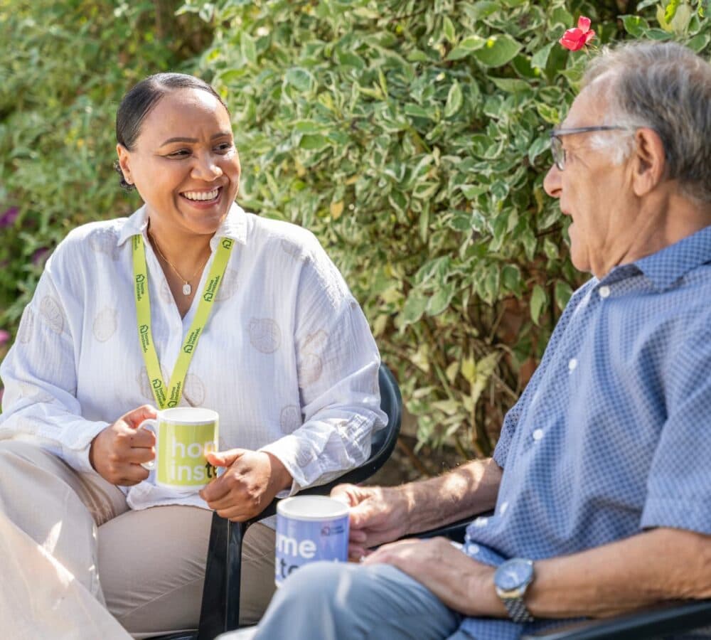 An older male adult having coffee with his younger female carer in the garden