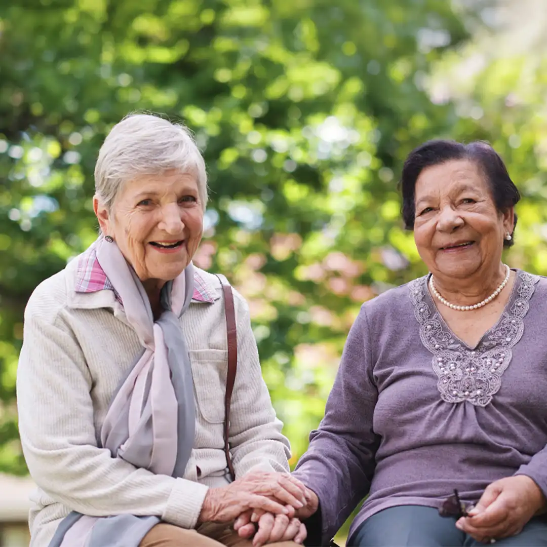 Two elderly ladies sitting and enjoying time together, holding each others hands.