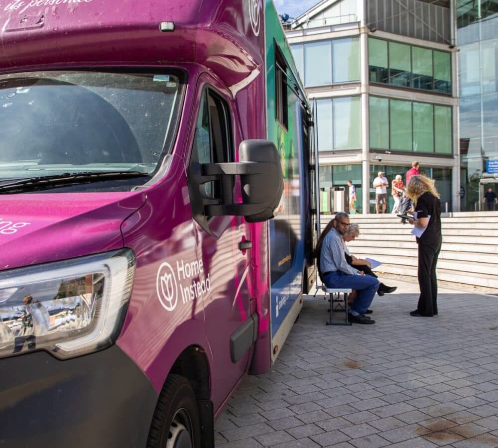 A big purple bus parked with some people beside it