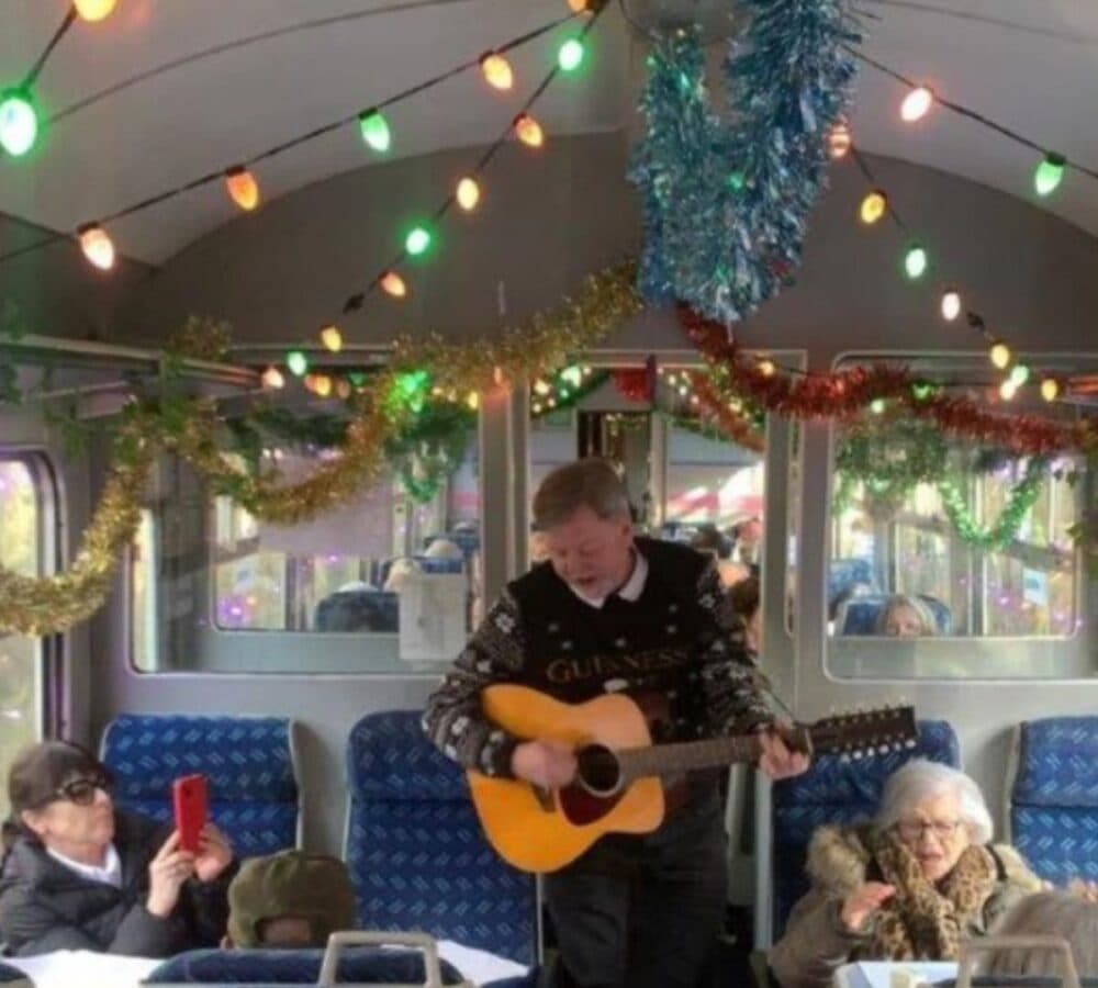 A man holding a guitar while singing inside the train while standing