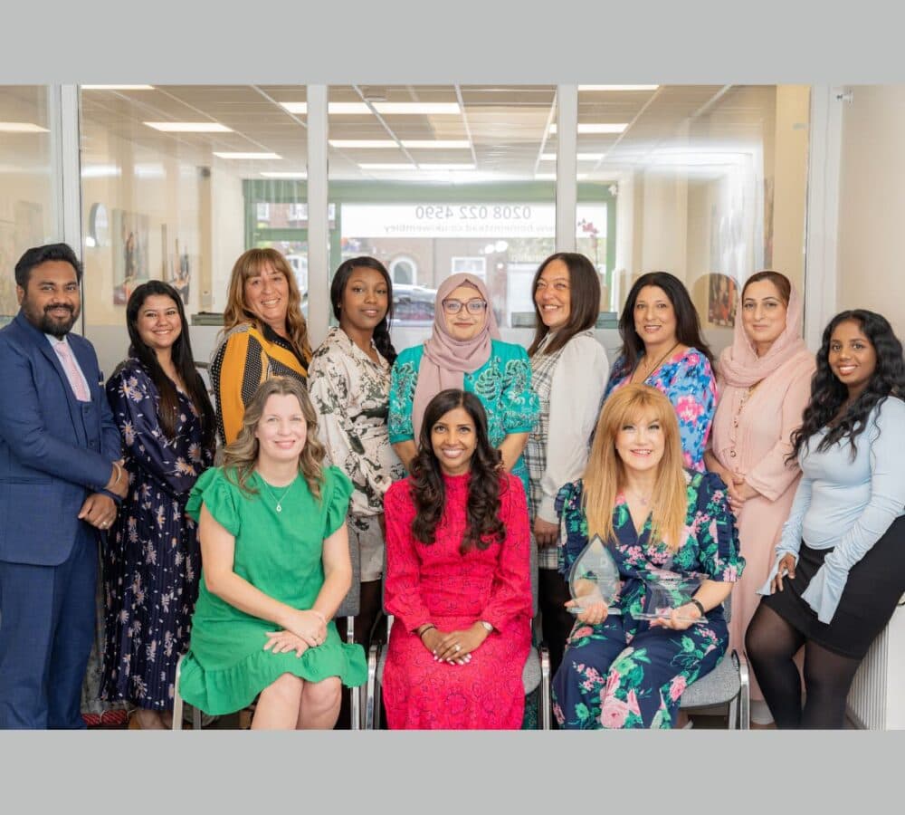 Team photo moslty women with one man all happy and smiling inside the office