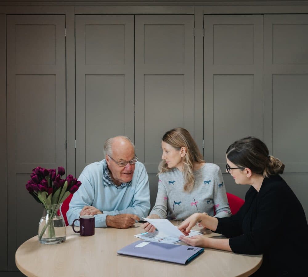 Three people discussing inside the house while sitting on a chair