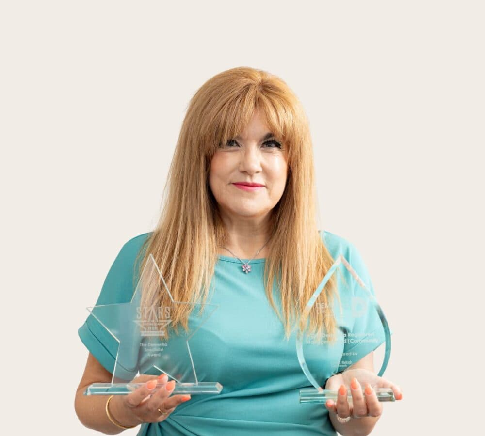 Woman with long blonde hair and wearing white gown happy and smiling while holding her plaque and award with a star lshaped light in the background