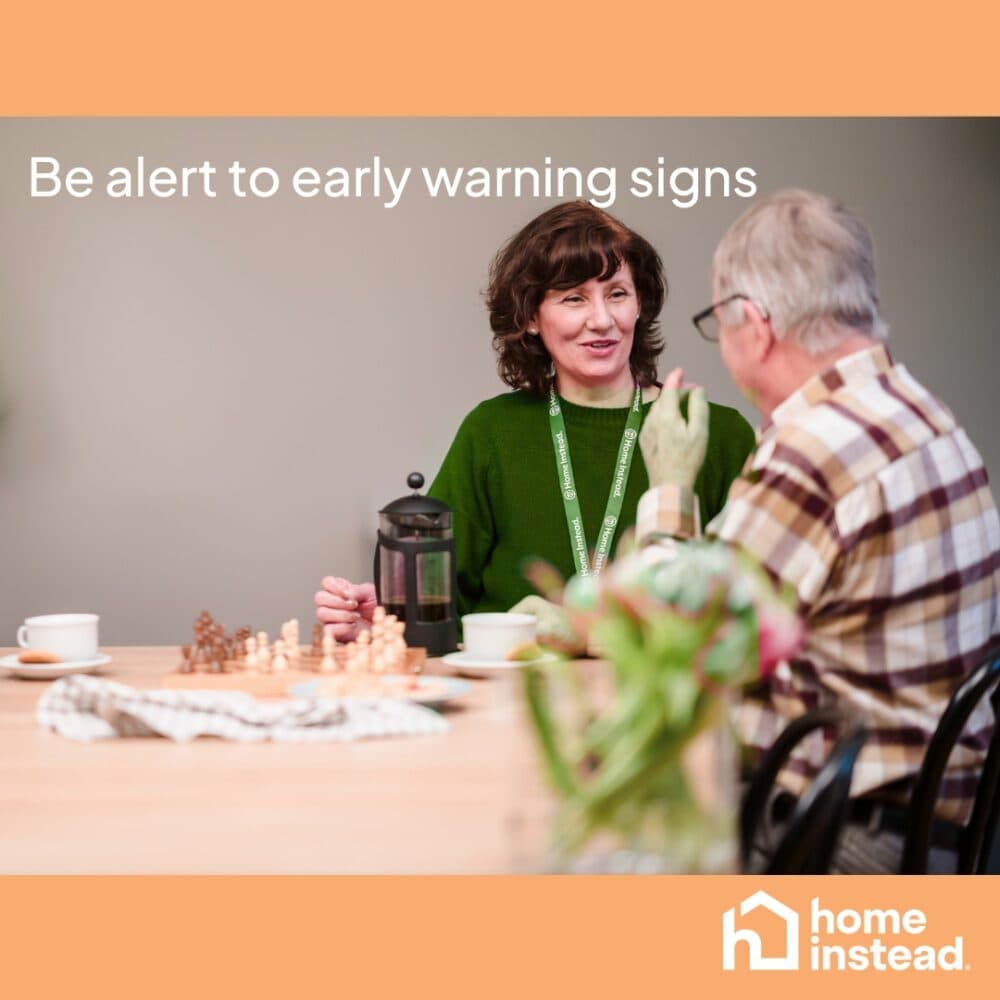 A woman and older man talk at a table; text reads "Be alert to early warning signs." Home Instead logo visible. - Home Instead
