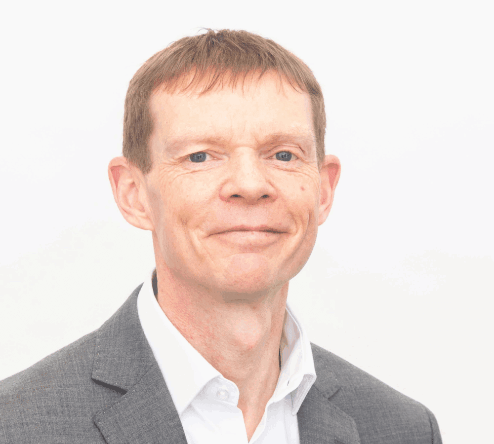 Smiling man in a gray suit and white shirt against a plain white background. - Home Instead