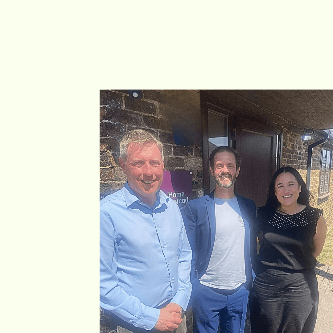 Three people smiling and standing outside a brick building on a sunny day. - Home Instead