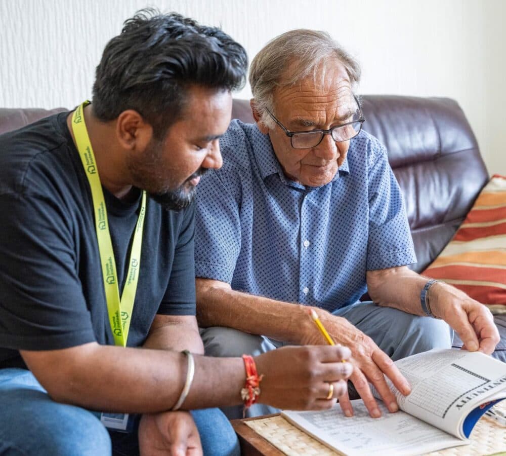 Two men sitting on a couch while doing puzzles