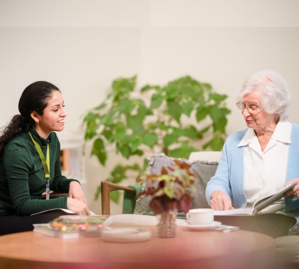 Two wome sitting on a coffee table while chatting and looking at a photo album inside the house