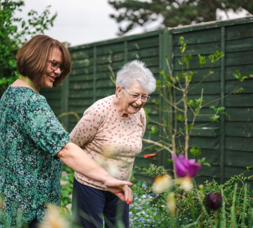 Two women both happy and smiling while looking at the flowers in the garden