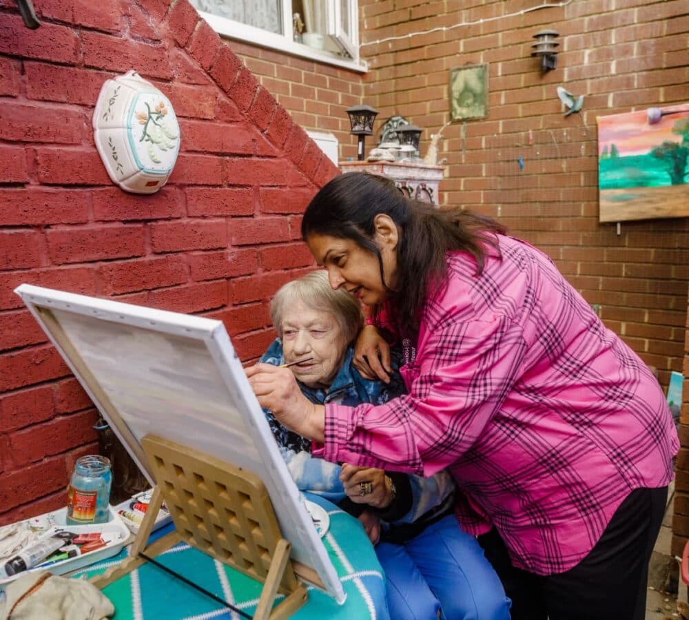 Two women painting together outside the house