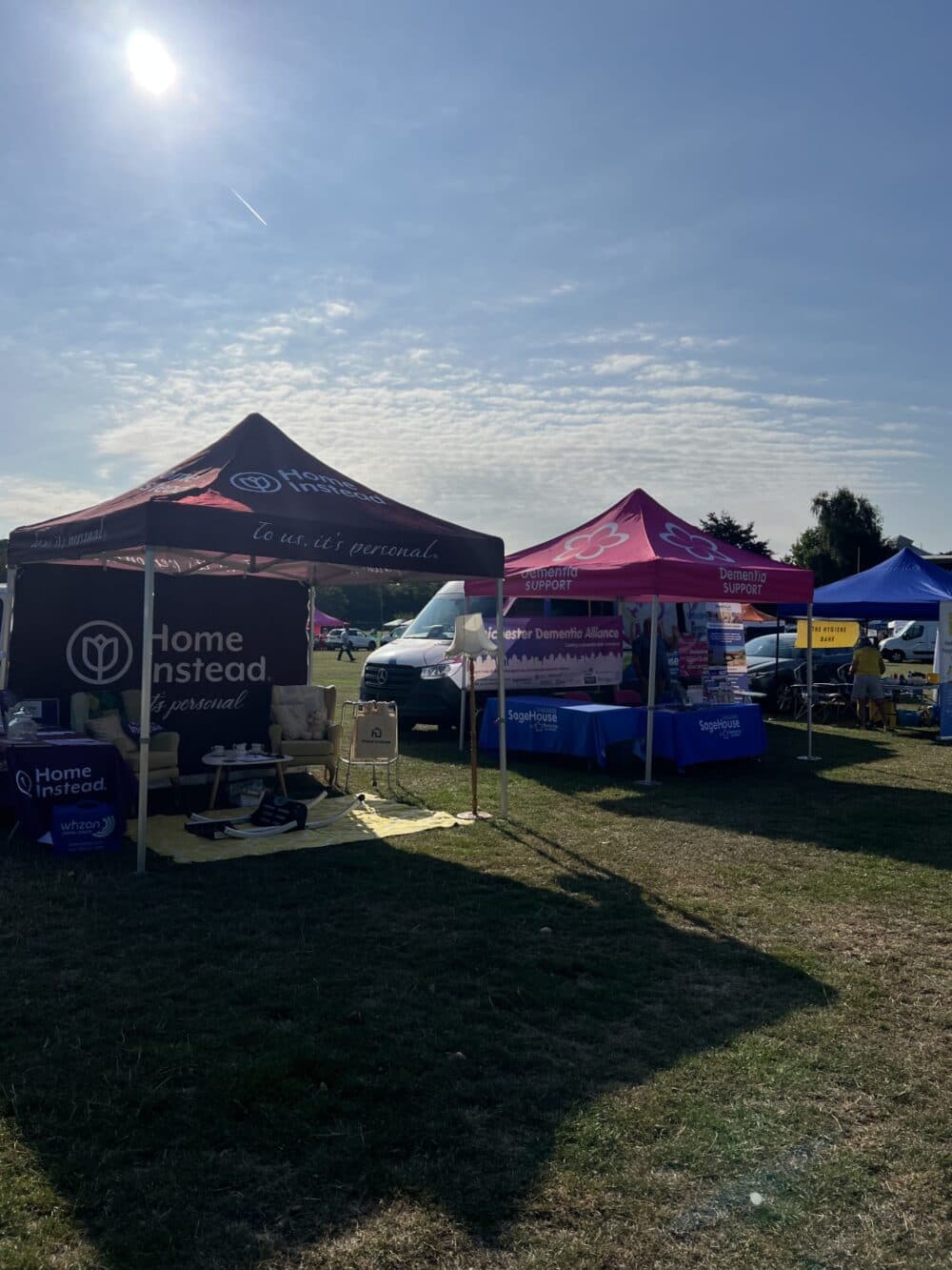 Outdoor event with several informational tents, including Home Instead and Dementia UK, on a sunny day. - Home Instead