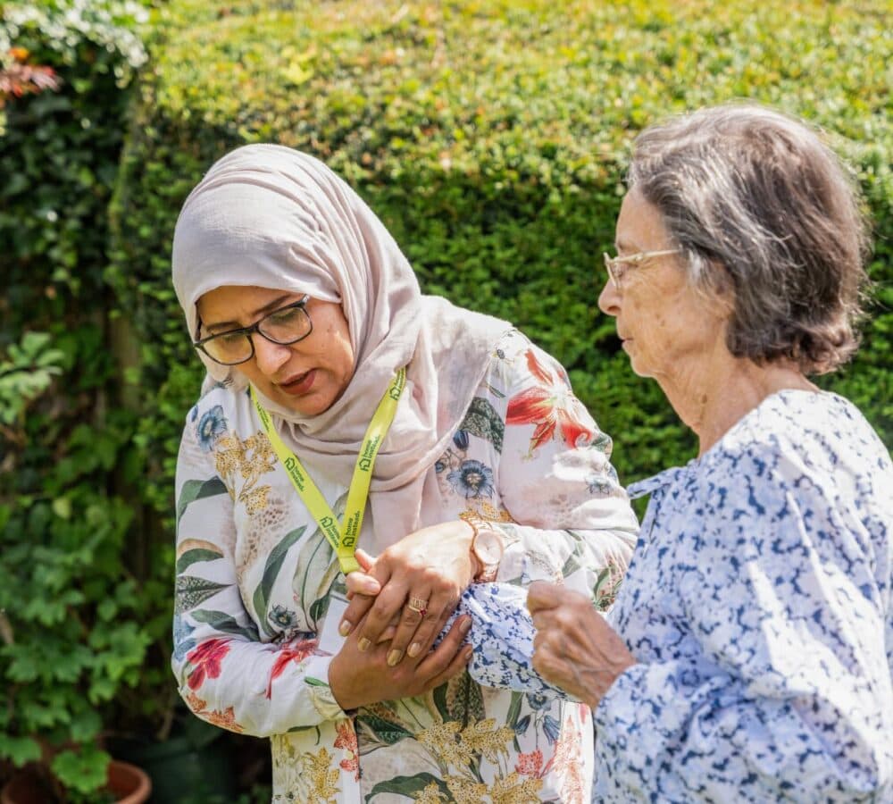An older female adult walking while being assisted by her younger female carer