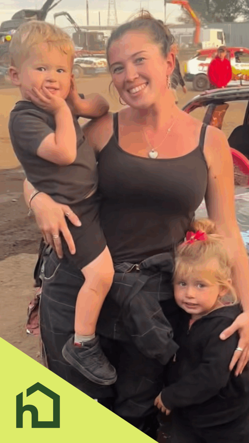 A smiling woman holds a young boy, with a young girl standing beside her, all dressed in black. - Home Instead