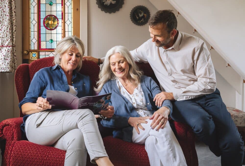Elderly woman sitting on a sofa with a younger woman on one side and a younger man on the other, looking happy