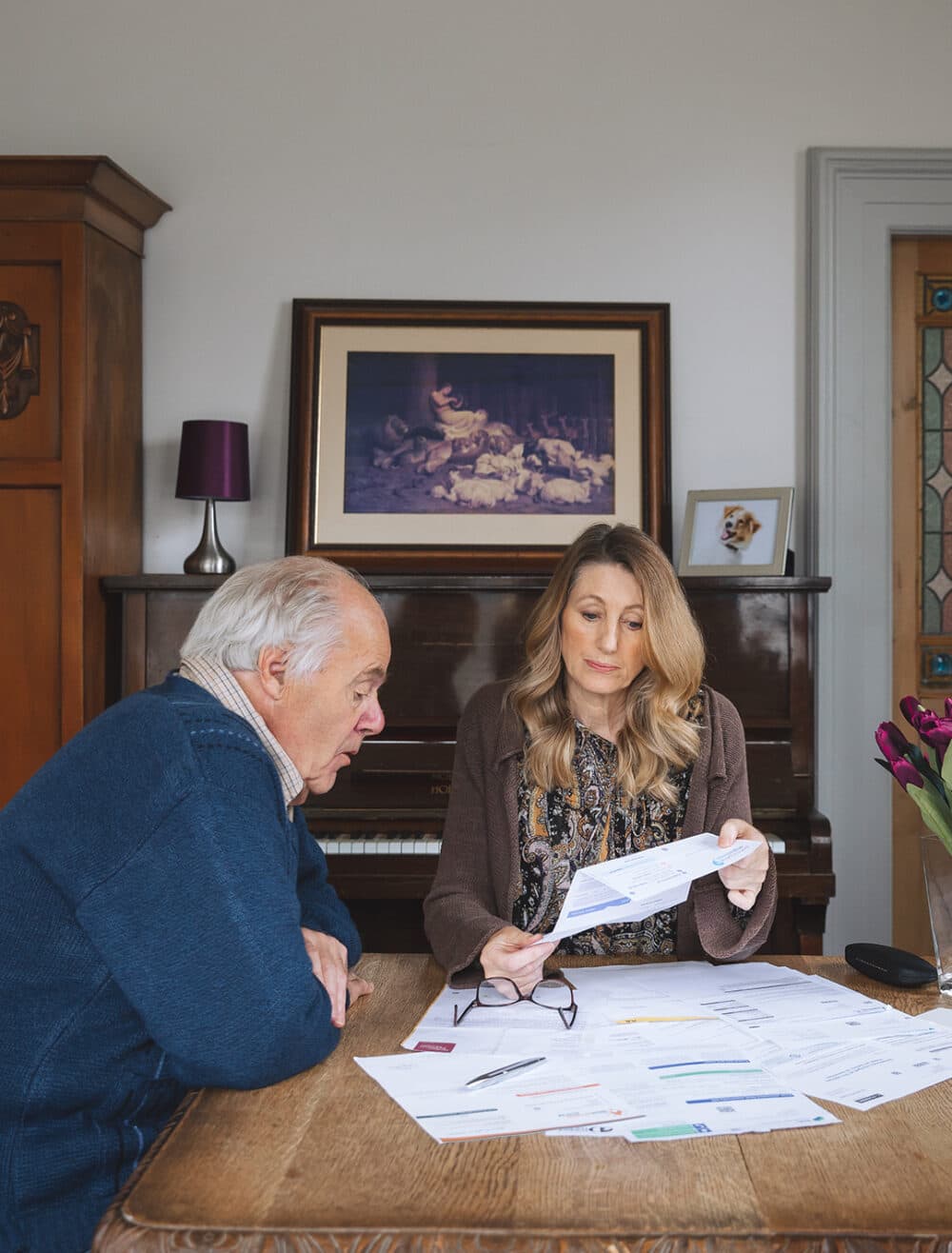 An older man and a woman review paperwork together at a wooden table in a cozy room. - Home Instead