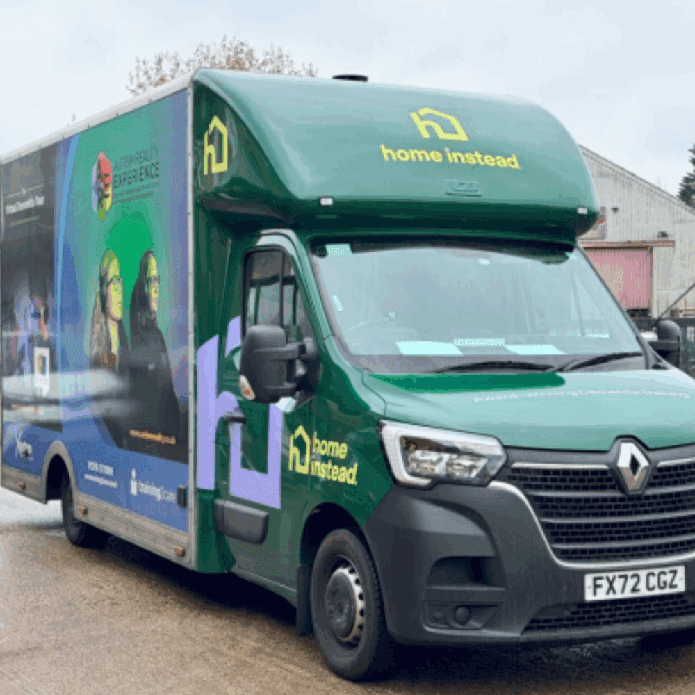 A green Home Instead van with branding and images parked outside on a wet day. - Home Instead