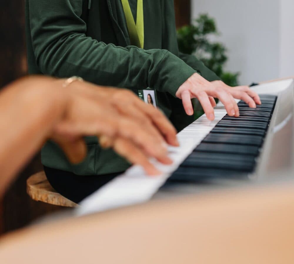 Two people playing piano together, focusing on their hands and piano keys. - Home Instead