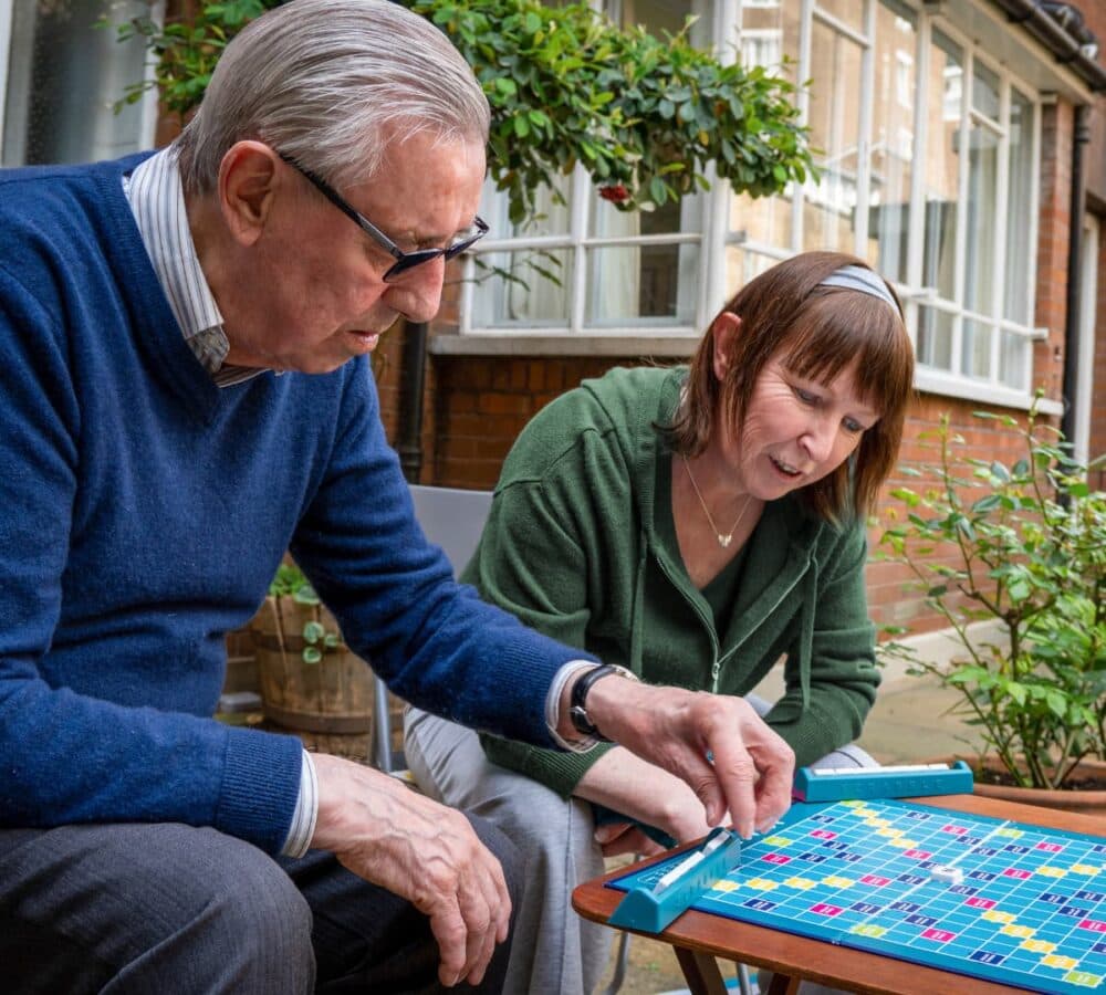 Two people playing scrabble together while sitting outside the house