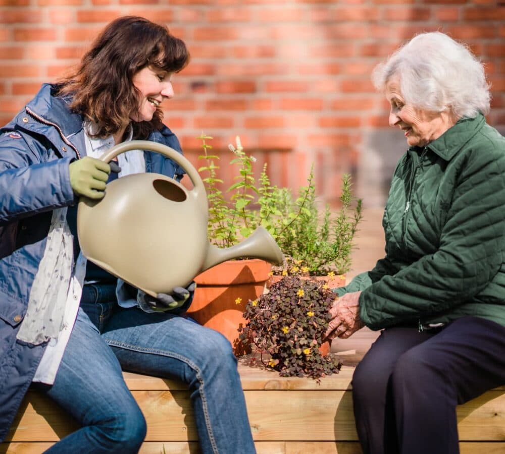 Two women happily watering plants outdoors Home Instead