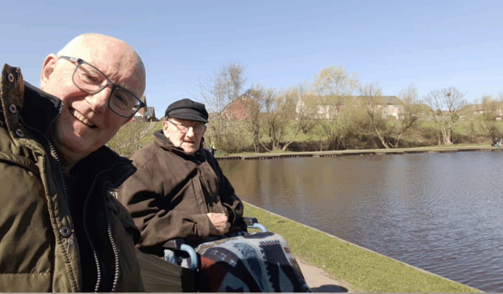 A man in a wheelchair by a river, then indoors at a fitness class with others. - Home Instead