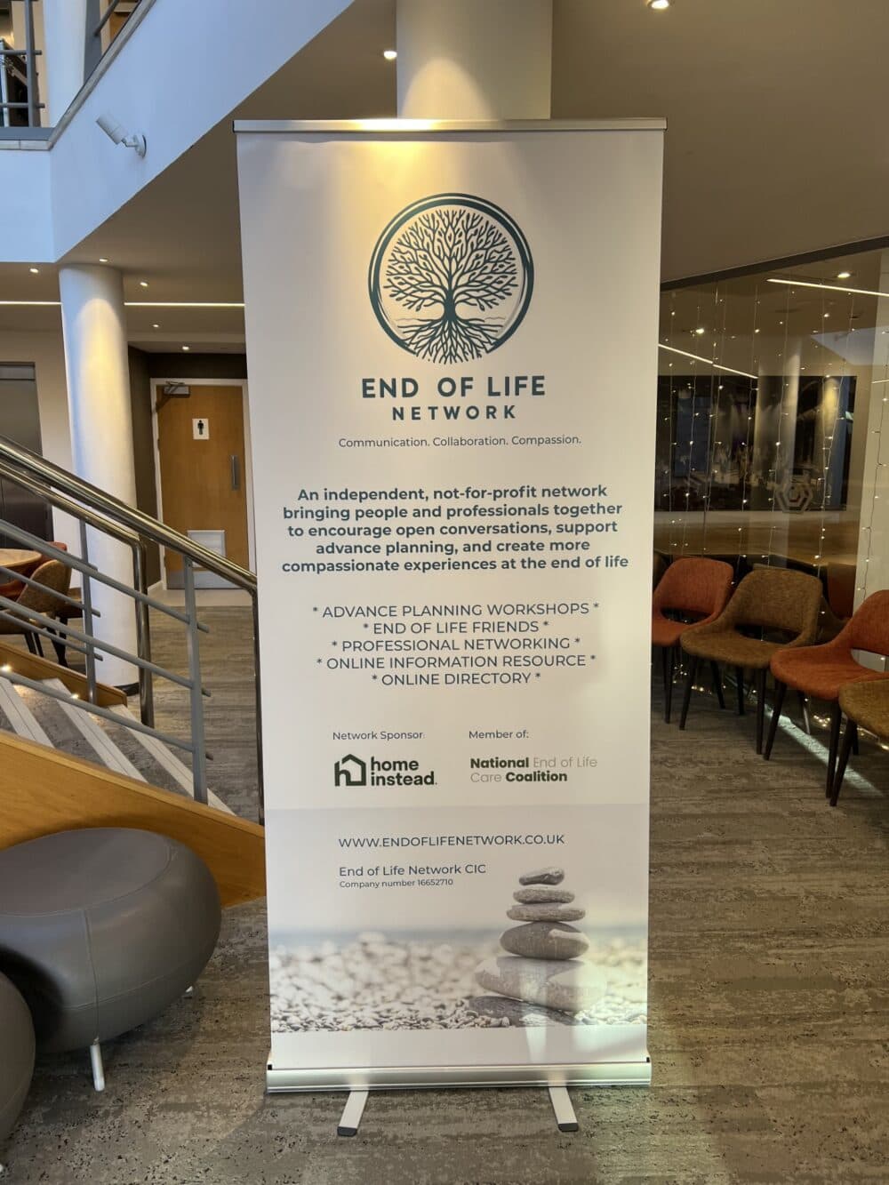 A standing banner for the End of Life Network with text about their support services in a modern lobby. - Home Instead