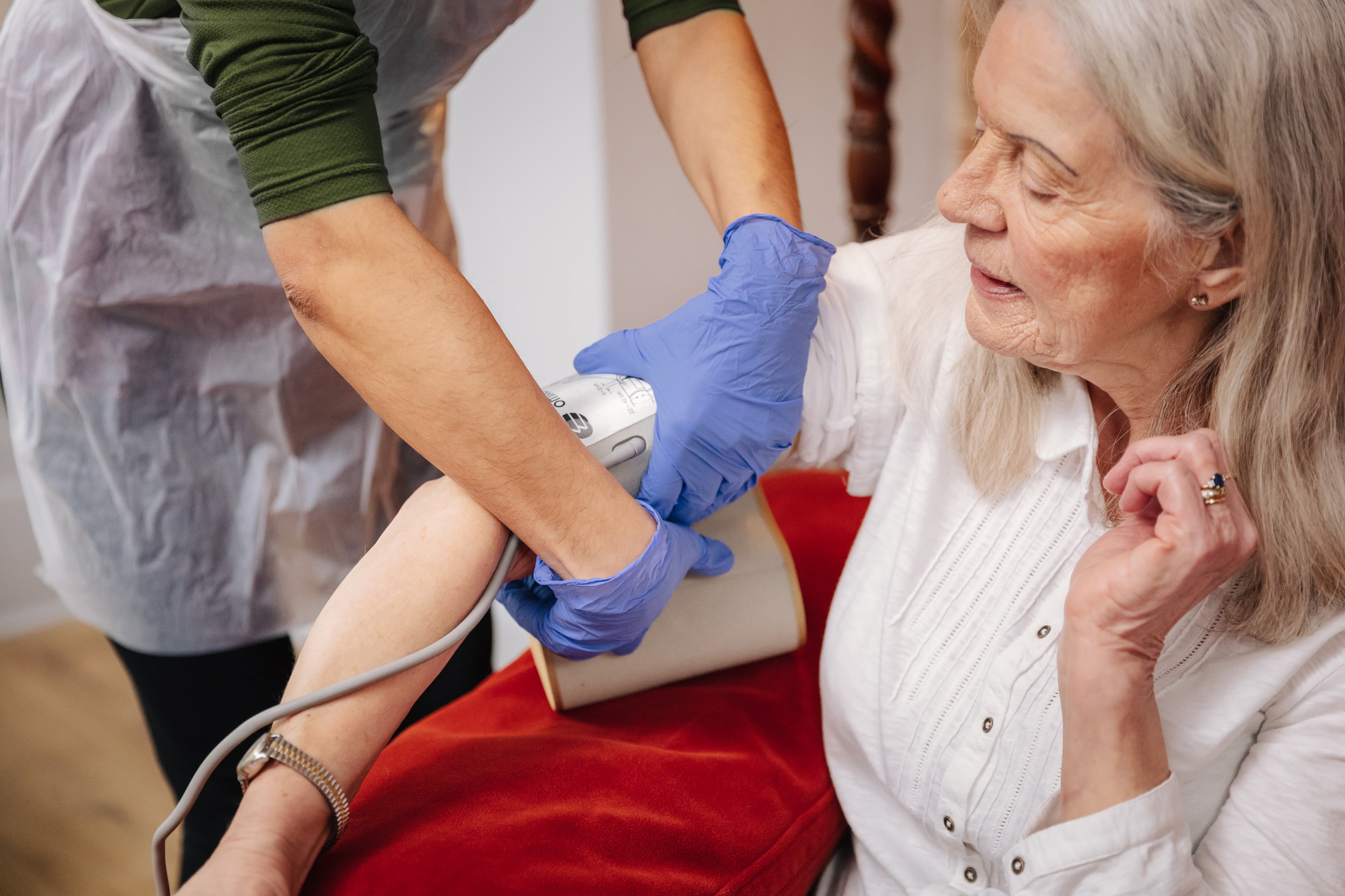 A nurse in gloves checks an older woman's blood pressure at home. - Home Instead