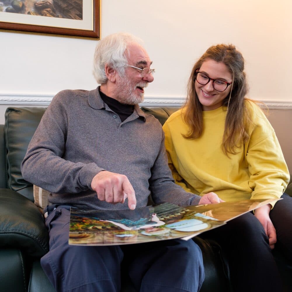 Male client sitting on sofa and looking at photographs with his granddaughter