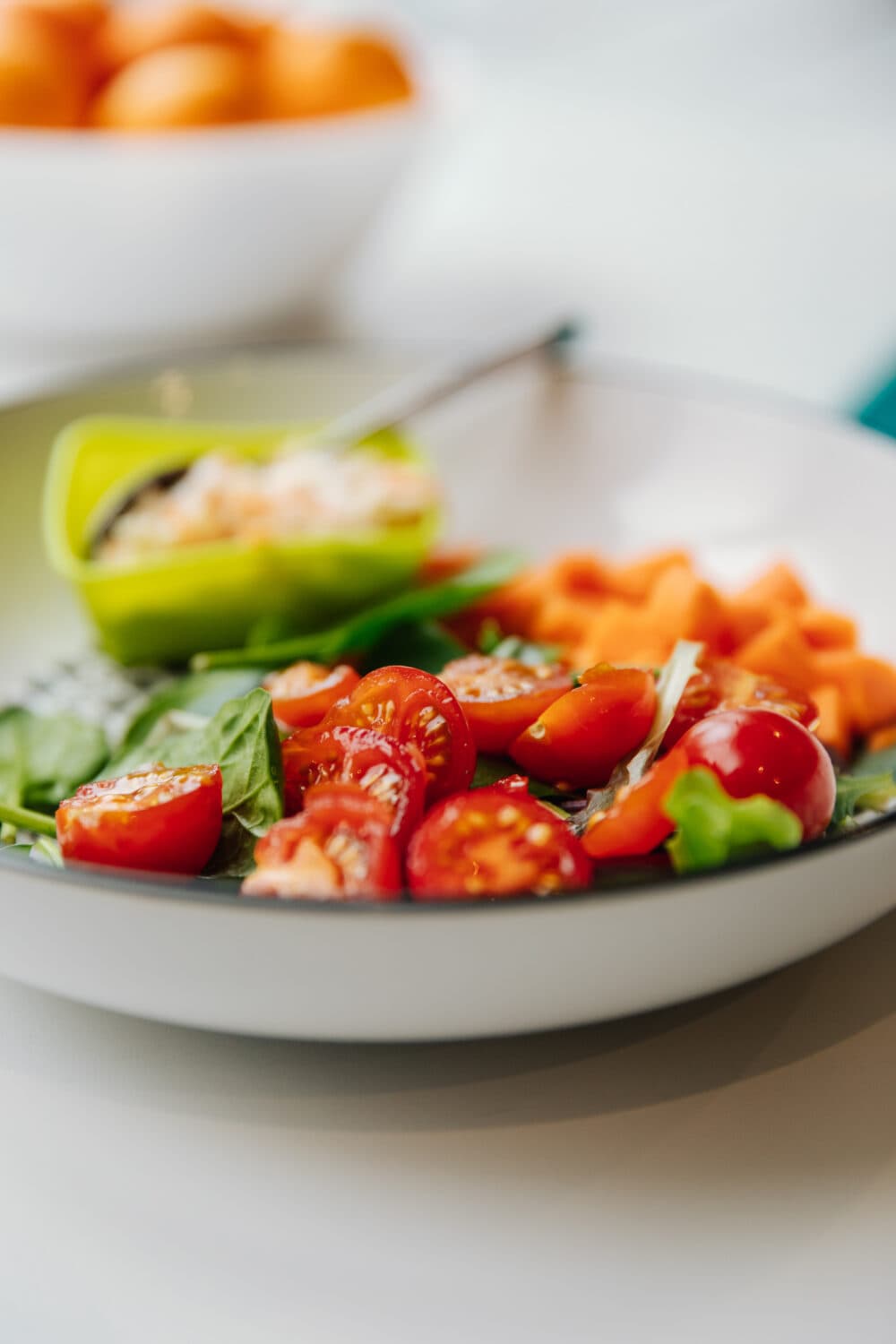 A plate of fresh salad with cherry tomatoes, spinach, and chopped carrots, with a small bowl of dip. - Home Instead