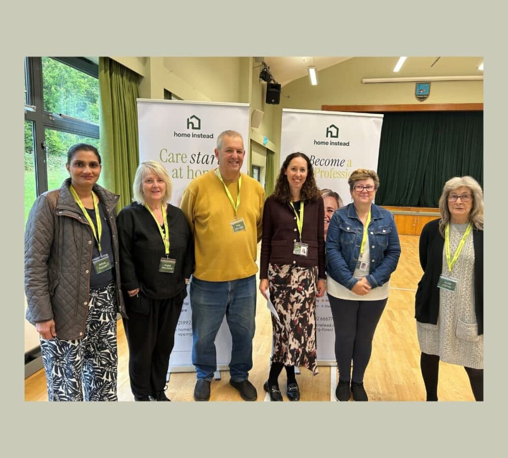 Group of men and women all happy and smiling while standing inside the hall - Home Instead
