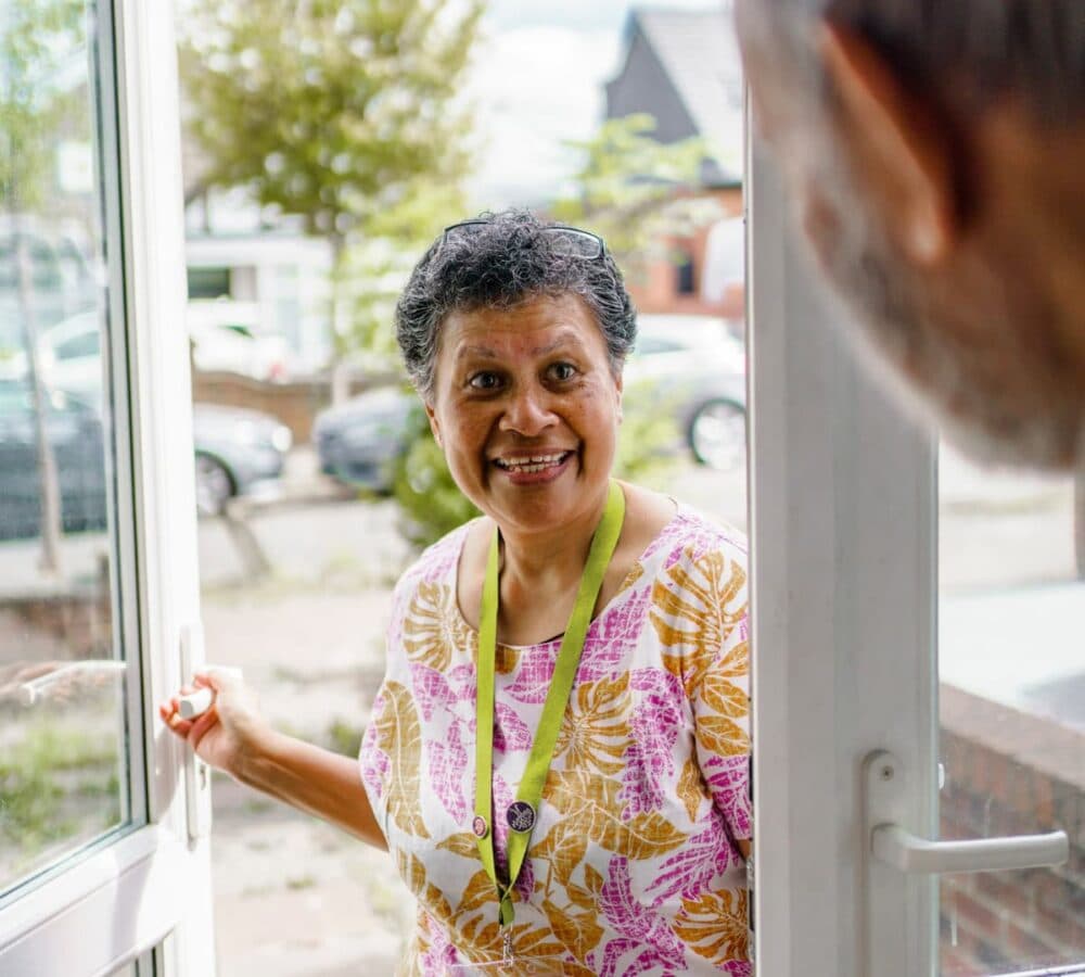 A female carer with grey hair happy and smiling while going inside the door