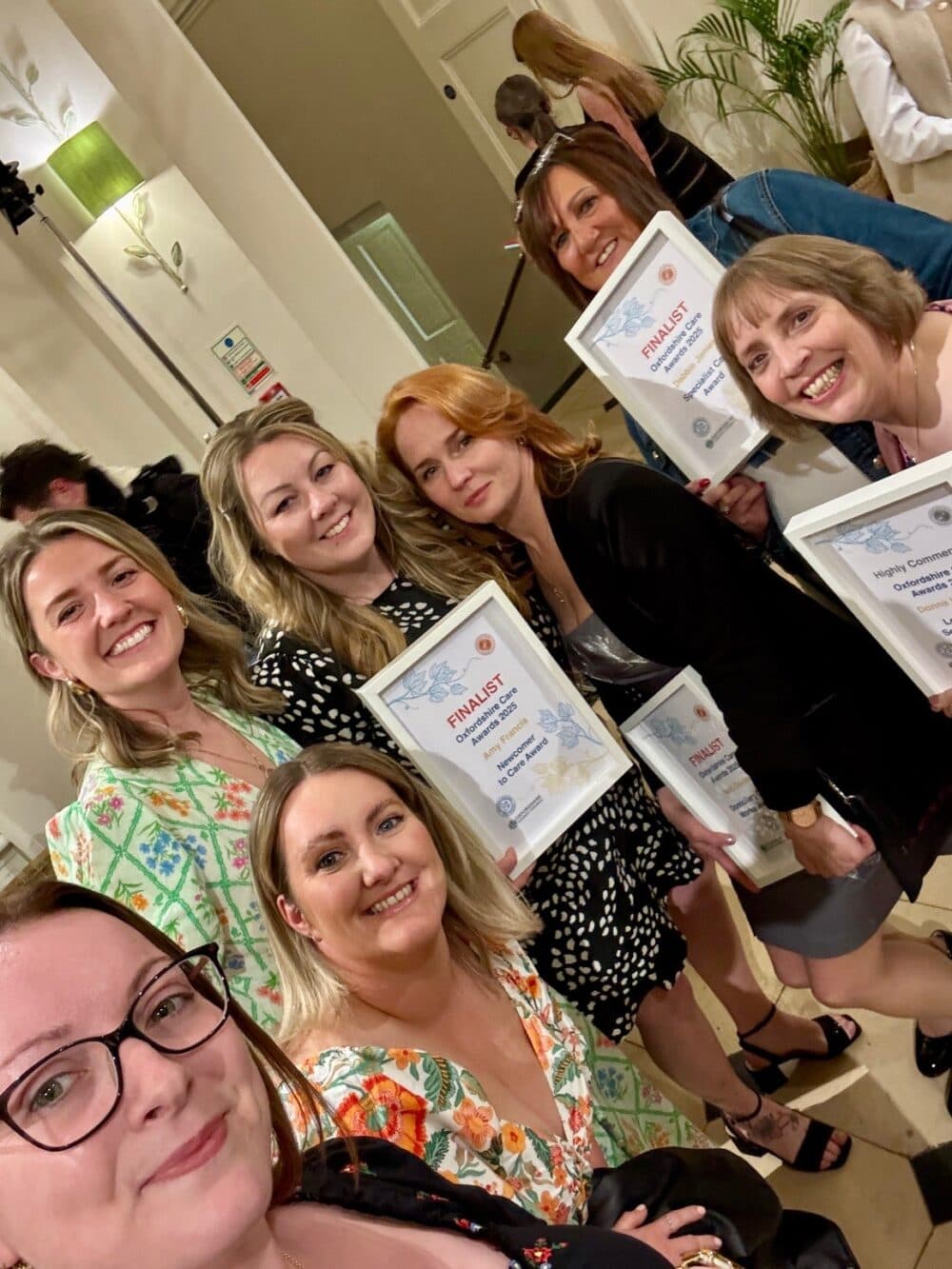 Six smiling women holding finalist certificates and posing together at an indoor event. - Home Instead