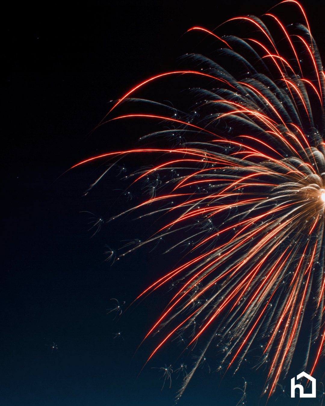 Red fireworks burst in the night sky with a small white house icon in the bottom right corner. - Home Instead