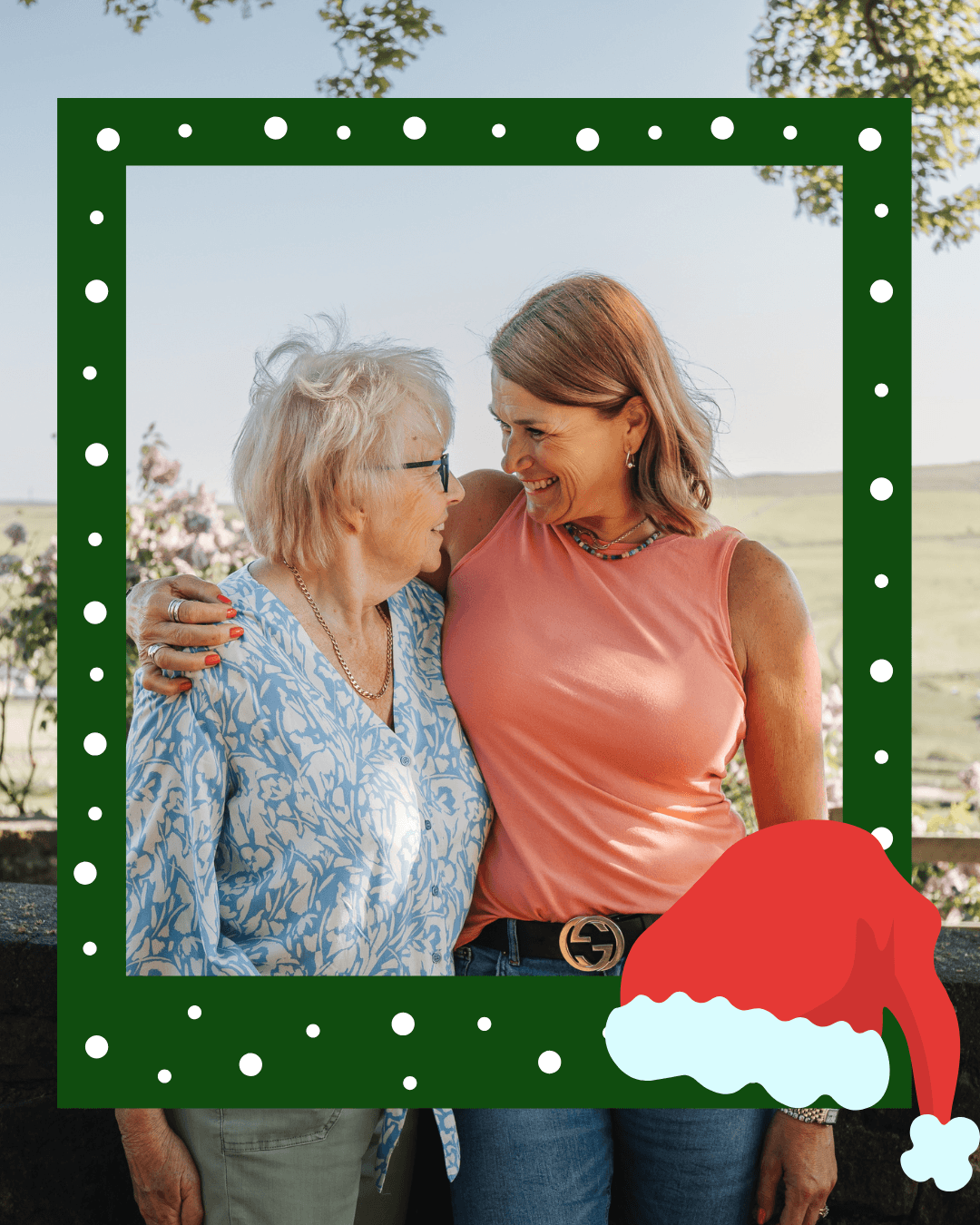 Two women smiling at each other, framed with a festive border featuring a Santa hat. - Home Instead