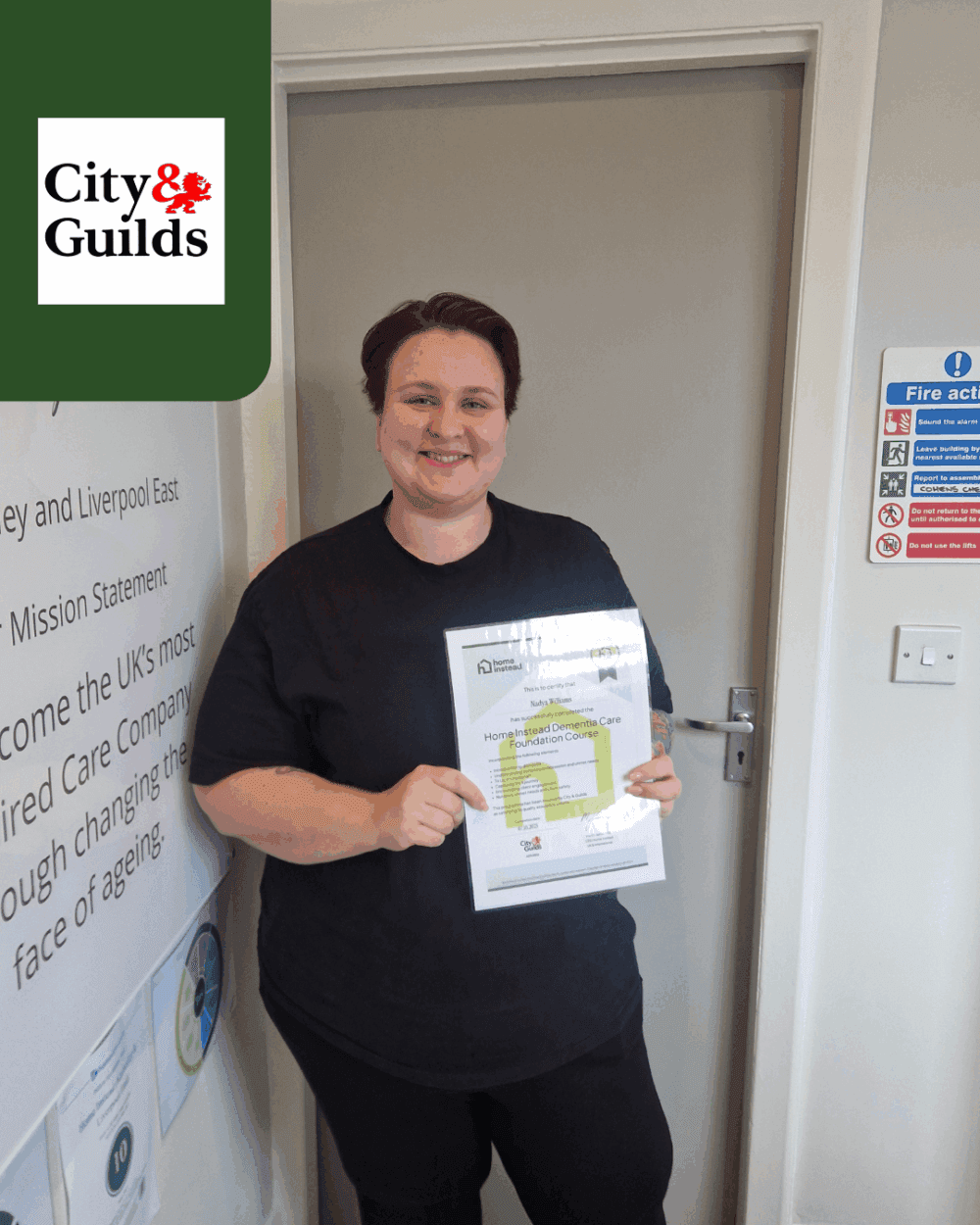 A person smiling and holding a certificate stands indoors near a door with City & Guilds logo in the corner. - Home Instead