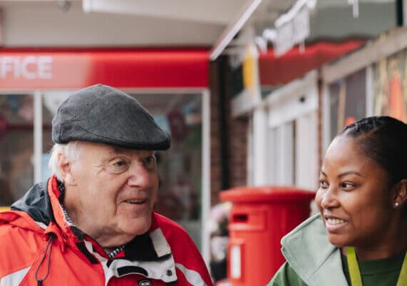 A Care Professional looking at an older adult in front of a post office