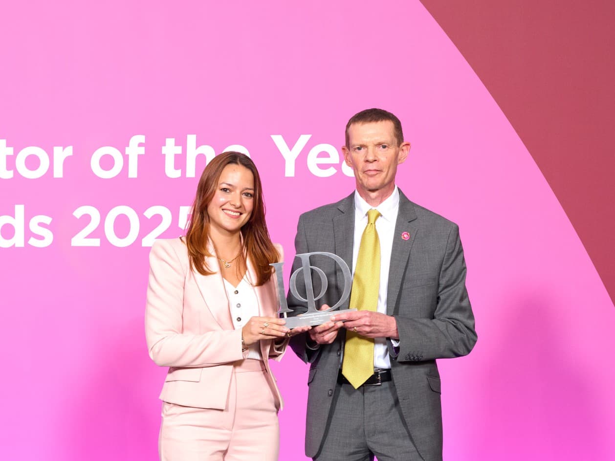 Two people in business attire smile and hold an award against a pink background with white text. - Home Instead